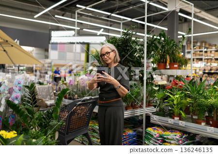 Senior woman shopping for plants in a modern garden center during the day 136246135