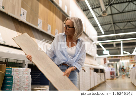 Woman in a home improvement store examines a laminate plank in the flooring section during the Woman in a home improvement store examines a laminate plank in the flooring section during the 136246142