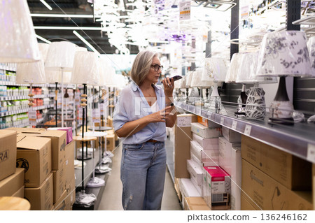Woman shopping for lamps in a home goods store while using a smartphone to check details 136246162