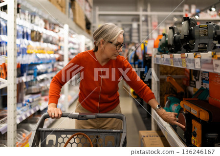 Older woman shopping for equipment in a hardware store during the daytime while examining a Older woman shopping for equipment in a hardware store during the daytime while examining a 136246167
