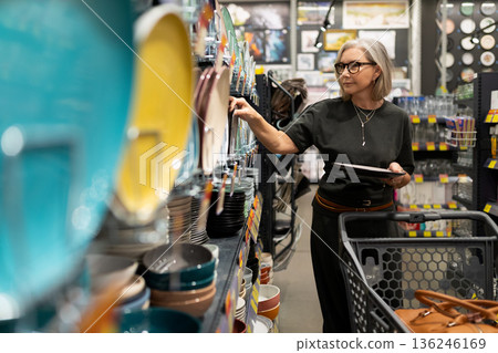 Senior woman shopping for dinnerware in a modern home goods store during the afternoon 136246169