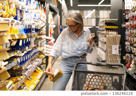 Woman shopping for paint supplies in a home improvement store aisle during midday 136246228