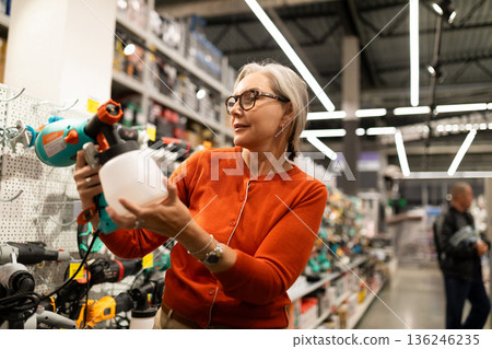 Woman examines a spray tool while shopping in a hardware store during the day 136246235