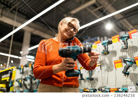 Elderly woman chooses tools in a hardware store while talking on the phone 136246238