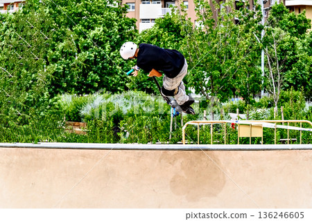 Young man practicing Scootering (Freestyle Scootering) in the new SkatePark in the central park of Igualada, Barcelona, Spain 136246605