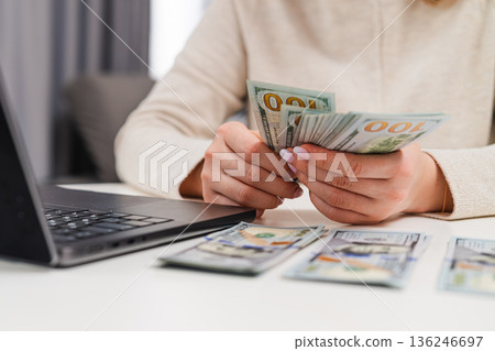 Woman counting us dollar banknotes while entering financial data on computer. Concept of accounting and personal finance management. Woman counting us dollar banknotes while entering financial data on computer. Concept of accounting and personal finance management. 136246697