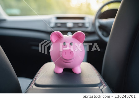 A pink piggy bank sits on the center console of a car. It is used to save money for car expenses. The vehicle is parked, and interior details are visible in the background. A pink piggy bank sits on the center console of a car. It is used to save money for car expenses. The vehicle is parked, and interior details are visible in the background. 136246701