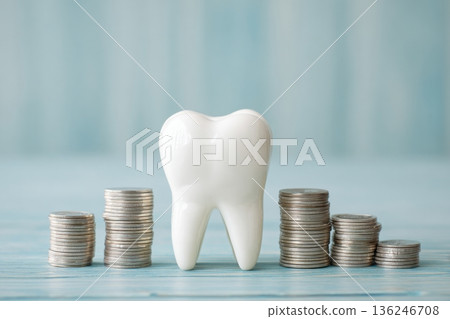 A white tooth figure stands in front of several stacks of coins on a light blue background. This visual illustrates the connection between dental care and the cost associated with it. 136246708