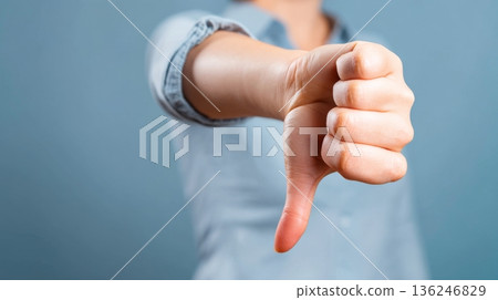 A hand is raised with the thumb pointed downward. The gesture signifies disapproval or dissatisfaction. The person is indoors with a plain background, indicating the individual's sentiment. A hand is raised with the thumb pointed downward. The gesture signifies disapproval or dissatisfaction. The person is indoors with a plain background, indicating the individual's sentiment. 136246829