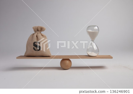 A balance scale displays a bag of money and an hourglass. The setting is indoors with a clean background. The image illustrates the relationship between financial wealth and time. A balance scale displays a bag of money and an hourglass. The setting is indoors with a clean background. The image illustrates the relationship between financial wealth and time. 136246901