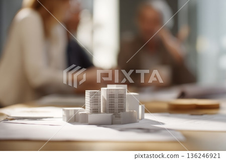 People are engaged in a discussion about a property development project. A model building is on the table while others share ideas in a well-lit office space. People are engaged in a discussion about a property development project. A model building is on the table while others share ideas in a well-lit office space. 136246921