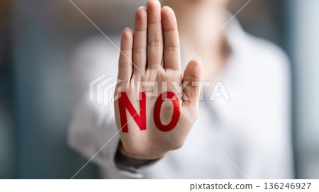 A hand is raised with the palm facing forward and the word NO printed in red. This gesture is common in conversations or meetings to express refusal or disagreement. 136246927