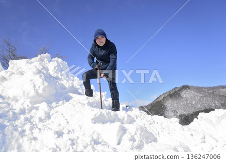 An elderly man undergoing rehabilitation by using a cane to go up and down snowy stairs 136247006
