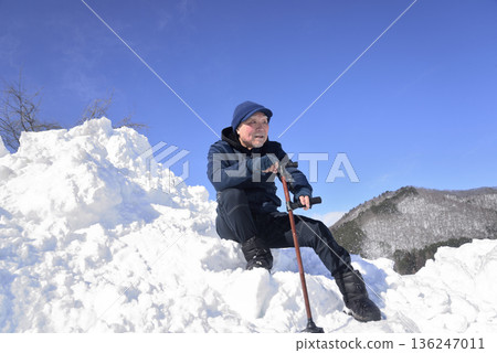 An elderly man undergoing rehabilitation by using a cane to go up and down snowy stairs 136247011