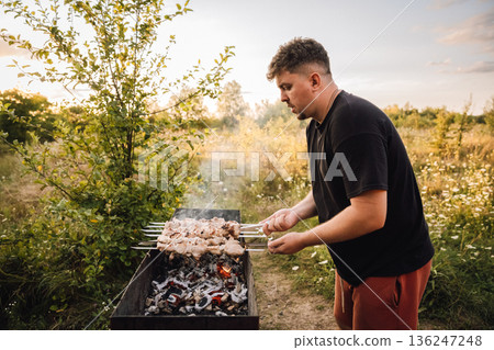 Man grilling pork shashlik over charcoal in countryside at sunset Man grilling pork shashlik over charcoal in countryside at sunset 136247248