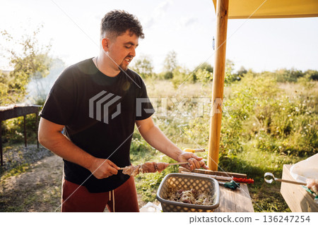 Man preparing meat skewers for outdoor barbecue at sunset, summer grilling in nature Man preparing meat skewers for outdoor barbecue at sunset, summer grilling in nature 136247254