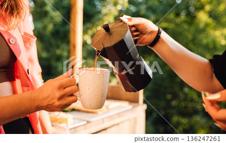 Moka pot pouring hot coffee into mug outdoors at sunset Moka pot pouring hot coffee into mug outdoors at sunset 136247261