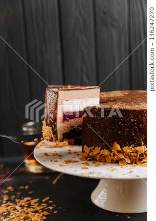 Layered chocolate mousse cake slice with raspberry jelly on spatula, dark background 136247270