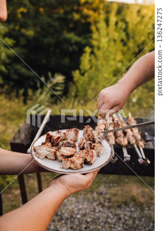Serving grilled pork shashlik from skewer onto plate at outdoor barbecue 136247275