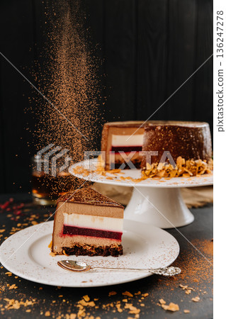 Layered chocolate mousse cake slice with berry layer and falling cocoa dust 136247278