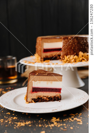 Chocolate mousse cake slice with berry layer on plate, cocoa dust, dark backdrop 136247280