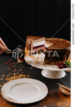 Layered chocolate mousse cake slice with raspberry jelly on spatula, dark background 136247283