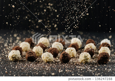 Assorted chocolate truffles with falling cocoa crumbs on dark background Assorted chocolate truffles with falling cocoa crumbs on dark background 136247288