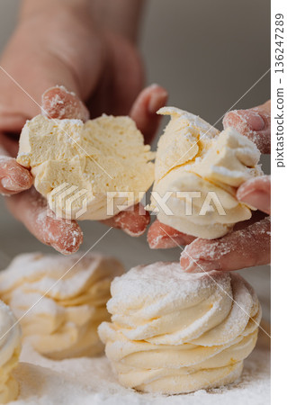 Hands breaking vanilla zephyr with powdered sugar, close-up homemade dessert 136247289