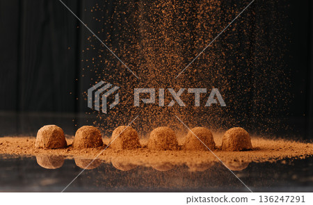 Cocoa powder falling over chocolate truffles with reflection on black background Cocoa powder falling over chocolate truffles with reflection on black background 136247291