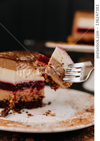 Fork with bite of layered chocolate mousse cake and berry jelly closeup Fork with bite of layered chocolate mousse cake and berry jelly closeup 136247303