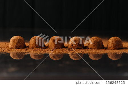 Cocoa dusted chocolate truffles in a row with reflection on black background 136247323