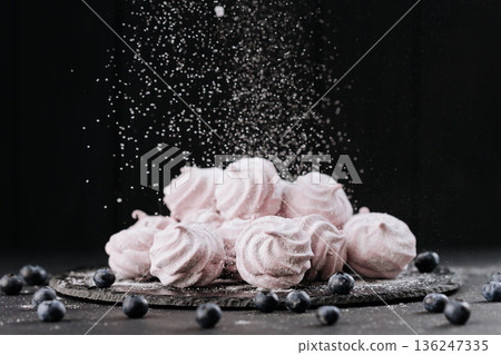 Pink meringue cookies with blueberries and falling sugar on slate, dark background Pink meringue cookies with blueberries and falling sugar on slate, dark background 136247335