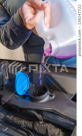 Person pouring purple liquid into a car's reservoir cap, showcasing automotive maintenance in a close-up view of the engine compartment Person pouring purple liquid into a car's reservoir cap, showcasing automotive maintenance in a close-up view of the engine compartment 136247722