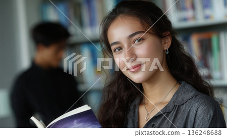 Young woman holding book in library 136248688