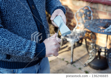 Man 's hand sharpening the kitchen knife with whetstone outdoor 136248885