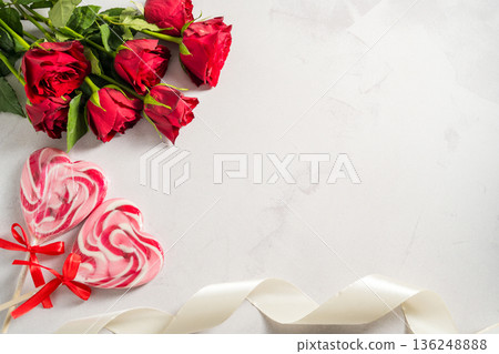 Valentine's Day background. Red roses and heart shaped lolly candy over grey background. Abstract flat lay. Celebrate, festive greeting card. Valentine's Day background. Red roses and heart shaped lolly candy over grey background. Abstract flat lay. Celebrate, festive greeting card. 136248888