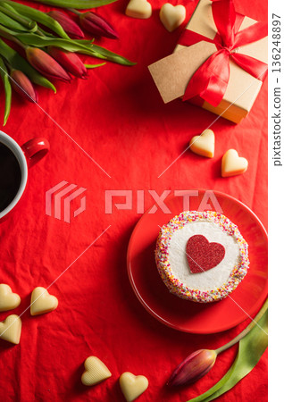 Valentine's Day frame background. Cake with red heart, cup of coffee, gift box, heart chocloales and spring red tulip flower bouquet. Top view Valentine's Day frame background. Cake with red heart, cup of coffee, gift box, heart chocloales and spring red tulip flower bouquet. Top view 136248897