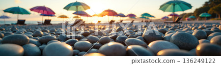 A pebble beach at sunset with colorful umbrellas. 136249122