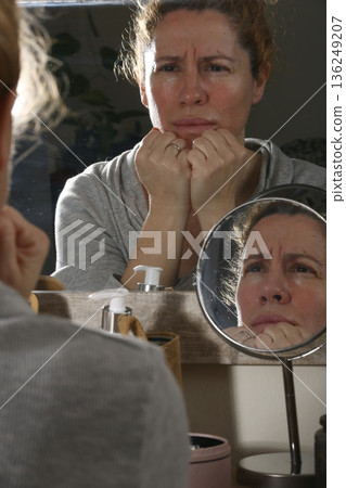 Mature Woman Practicing Face Yoga in Front of Mirror Mature Woman Practicing Face Yoga in Front of Mirror 136249207