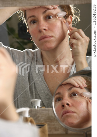 Mature Woman Practicing Face Yoga in Front of Mirror Mature Woman Practicing Face Yoga in Front of Mirror 136249219
