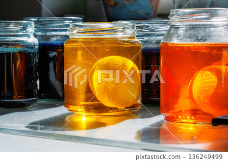 Close up of a easter egg in a yellow and orange food dye solution in a glass jars on a sunlit kitchen table 136249499
