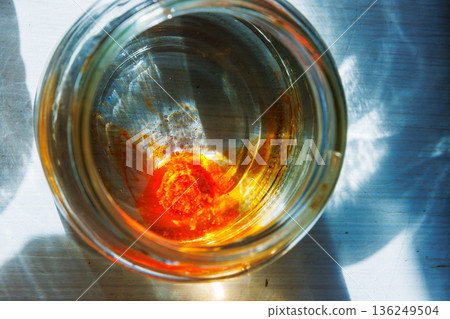 Top view into a glass jar of water with an orange food dye tablet dissolving at the bottom 136249504