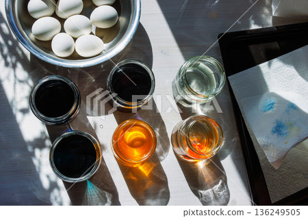 Top view of easter egg dyeing setup with eggs and glass jars with colored water in sunlight Top view of easter egg dyeing setup with eggs and glass jars with colored water in sunlight 136249505
