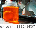 Egg soaking in orange food dye jar on sunlit kitchen table 136249507