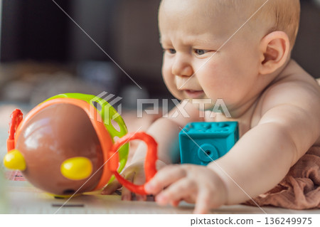 Little baby playing with toys on a soft baby play mat at home. Early childhood development, sensory play, learning through play, curiosity, and happy infant activity concept for modern parenting. 136249975