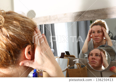 Mature Woman Practicing Face Yoga in Front of Mirror Mature Woman Practicing Face Yoga in Front of Mirror 136250413