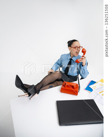 Young angry white woman in office attire working talking on vintage red phone, isolated on white background. In a blue shirt with a tie. Business occupation. Boss . Young angry white woman in office attire working talking on vintage red phone, isolated on white background. In a blue shirt with a tie. Business occupation. Boss . 136251508