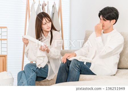 一對夫婦在客廳裡疊衣服(潮濕,有股霉味,在室內晾曬) 一對夫婦在客廳裡疊衣服(潮濕,有股霉味,在室內晾曬) 136251949