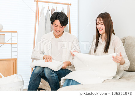 一對面帶著微笑的夫婦在客廳裡疊衣服（參與家務，分擔家務） 136251978