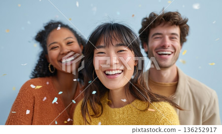 Diverse group of happy young adults smiling with falling confetti, embracing concepts of celebration, friendship, and success against a light blue background 136252917